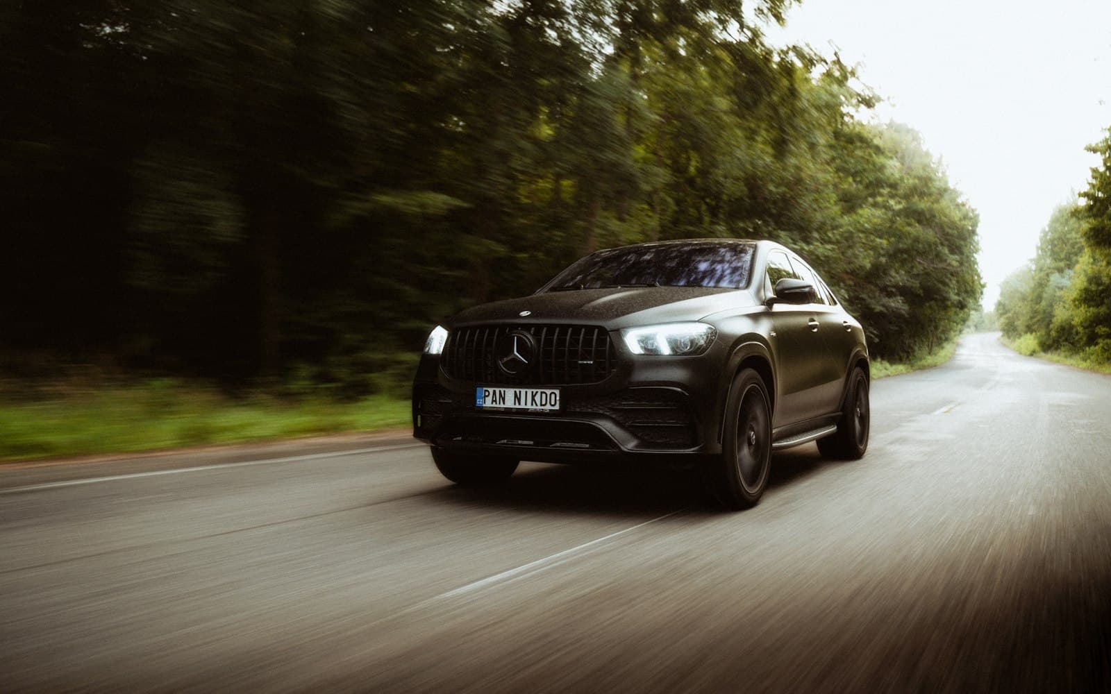 Black Mercedes-Benz GLE driving down a tree-lined road