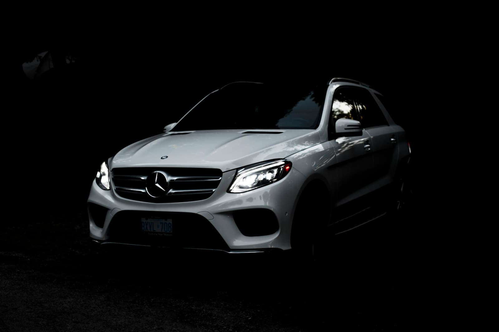 White Mercedes-Benz GLE SUV with headlights on against a dark backdrop