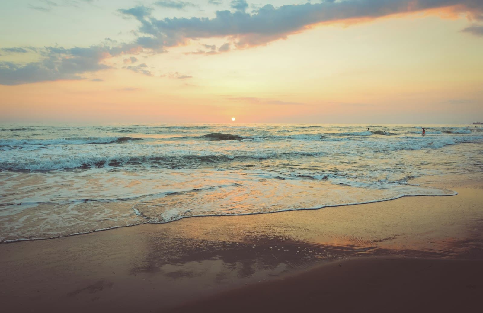 Waves washing ashore under an orange and pink sunset